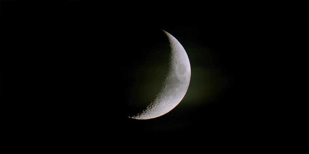 Der Mond zeichnet sich bei Nacht ab. Etwa ein Drittel der abgebildeten Kreisfläche ist durch die Sonne angestrahlt. Vor dem Mond zeichnet sich ein Schleier einer Wolke ab. Die Struktur des Mondes ist gut erkennbar im Spielfilm »Im Meer der Stille«.