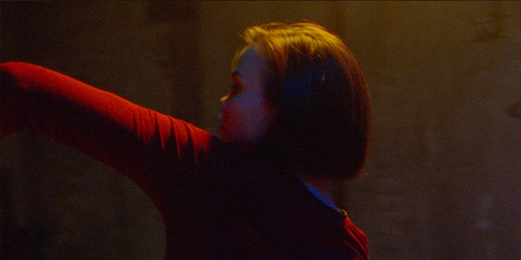 Eine Gläubige (Tatiana Feldman) tanzt in einer Kapelle. Sie trägt ein rotes Kleid. Ihren linken Arm streckt sie nach oben.