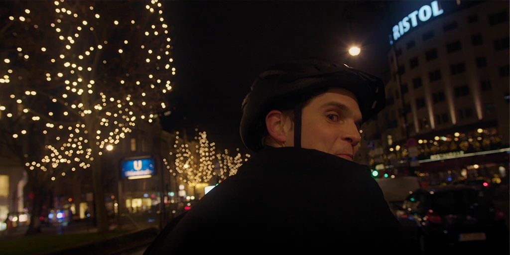 Ein junger Mann (Benjamin Lillie) fährt auf einem Tandem über den Kudamm. Er blickt in die Kamera. Die Bäume auf dem Mittelstreifen sind weihnachtlich beleuchtet im Werbespot »True Romance«.