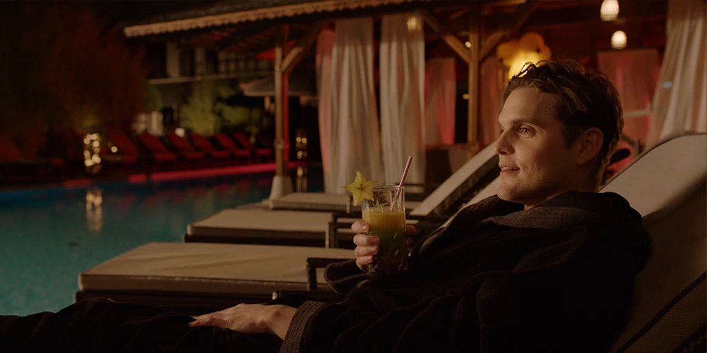 Louis (Benjamin Lillie) sitzt tiefenentspannt auf seiner Liege in einem Spa und schlürft einen Cocktail. Er trägt einen braunen Bademantel und befindet sich in einer gemütlichen Atmosphäre im Werbespot »True Romance«.