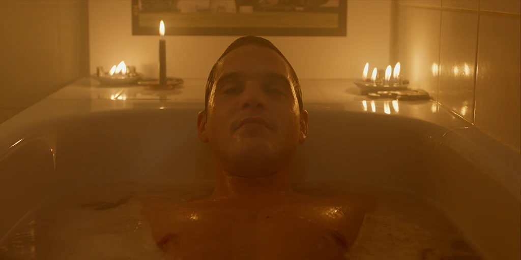 Louis (Benjamin Lillie) liegt bei Kerzenschein in der Badewanne und schaut in die Kamera. Hinter ihm befindet sich eine Kunstfotografie im Werbespot »True Romance«.