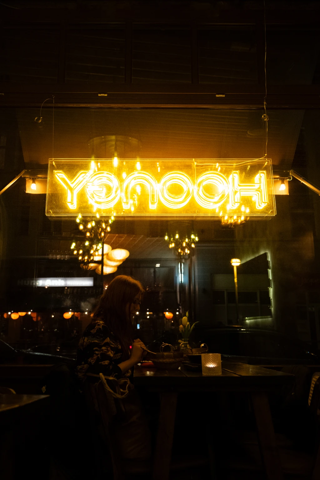Eine Frau sitzt in einem Restaurant unter einem gelben Neonschild und isst.