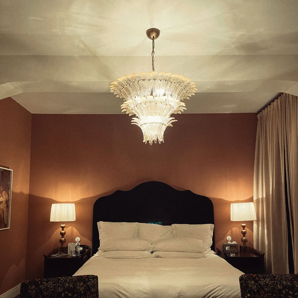 Ein Bett in einem schicken Hotelzimmer mit braunen Wänden. Im Vordergrund stehen zwei Sessel.
