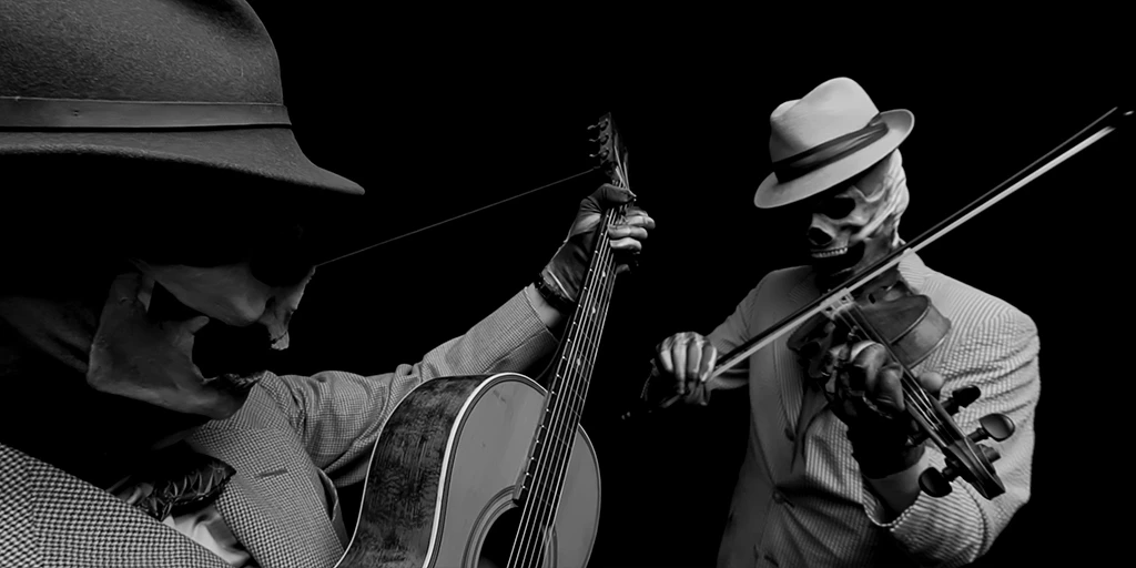 Sehr nah steht links ein Gitarrist der ein StÃ¼ck auf seiner Gitarre spielt. Er trÃ¤gt einen dunklen Hut und trÃ¤gt eine Totenkopfmaske. Rechts von ihm steht, mit etwas mehr Entfernung, ein Geiger. Er spielt auf seiner Geige und trÃ¤gt ebenfalls eine Totenkopfmaske sowie einen hellen Hut.
