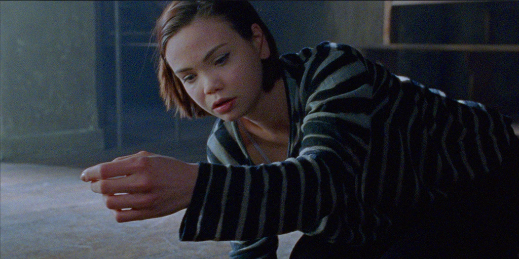 Eine junge Frau (Tatiana Feldman) sitzt auf dem Kapellenboden und betrachtet ihren Arm.